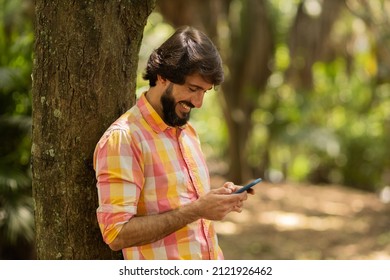 View of young man using a smartphone at day time with a green park in the background. Mobile phone, technology, urban concept. High quality photo