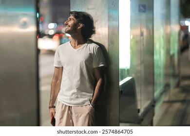  View of young man using a smartphone at night time with city view landscape in the background.