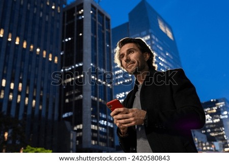 View of young man using a smartphone at night time with city view landscape in the background. High quality photo. 