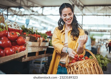 View at young woman buying vegetables at the market. A woman shops in a local outdoor agriculture market with fresh, organic local fruits and vegetables. She smiles as she compares different vegetable