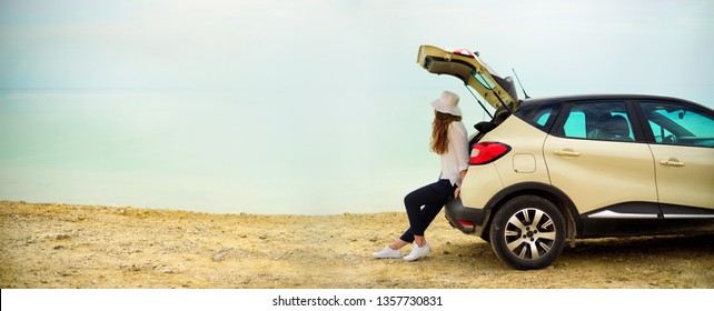 View Of Young Woman Traveler Looking At Sea Sunset, Sitting On Hatchback Car With The Copy Space. Banner.