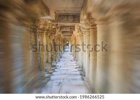 Viewed from the entrance, a zoom blur photo of ancient stone columns in a long temple passageway near Angkor Wat, Cambodia.