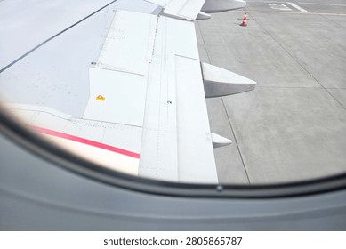 Viewed through an airplane window, this image features the aircraft's wing and a portion of the runway. the composition highlights the experience of air travel, emphasizing aviation and flight themes popular with travelers and aviation enthusiasts.