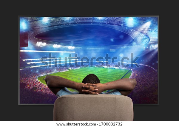 Viewer in front of a large TV relaxed on the\
armchair at home watching a sports\
game