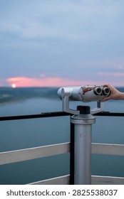 Viewing binoculars on an observation deck overlooking a lake at sunset.