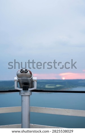 Viewing binoculars on an observation deck overlooking a lake at sunset.