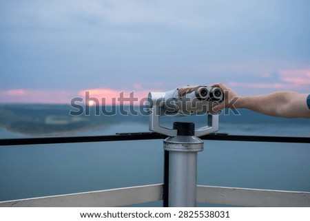 Viewing binoculars on an observation deck overlooking a lake at sunset.