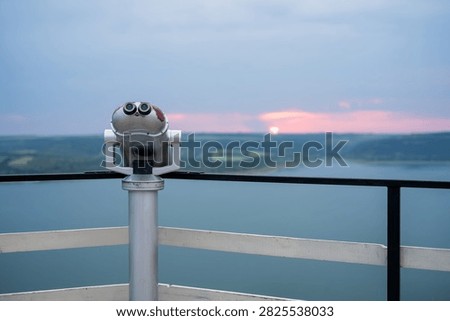 Viewing binoculars on an observation deck overlooking a lake at sunset.