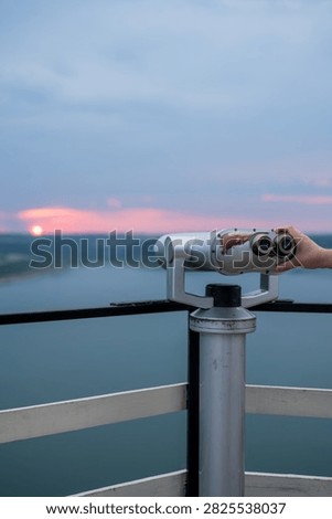 Viewing binoculars on an observation deck overlooking a lake at sunset.