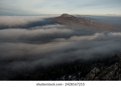 Viewing a cloudcovered mountain from the top creates a mystical atmosphere with fog blending into the sky, showcasing the majestic natural landscape of mountainous landforms