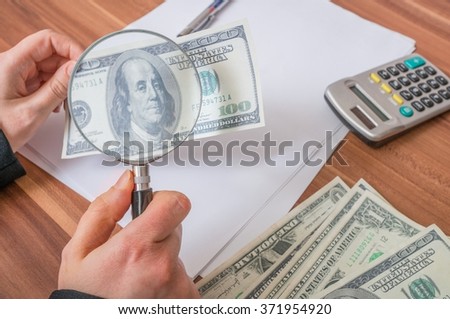 Viewing fake or counterfeit dollar banknote with magnifying glass.