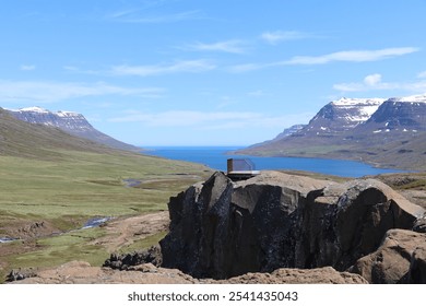 viewing platform on top of a rock formation overlooking a mountain stream and a panoramic view of the green mountains and blue fjord in the distance - Powered by Shutterstock