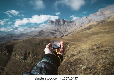 Viewpoint shot. A first-person view of a man's hand holds a compass against the background of an epic landscape with cliffs hills and a blue sky with clouds