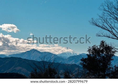 The viewpoint at the summit of Mount Takao, offering a beautiful view of overlapping mountain ranges and Mount Fuji with clouds obscuring its peak.