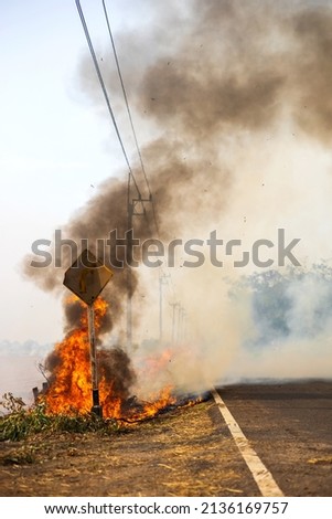 Views of blazes, burning hay, producing black clouds of black smoke, are blown by the wind, causing air pollution and potentially damaging paved road signs, a common sight in rural Thai farming.