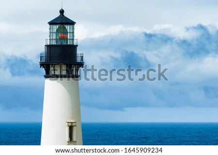 Views of the upper tower of Yaquina Head Lighthouse against cloudy skies over the Pacific Ocean