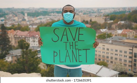 Vigorous ecology activist in respiratory mask striking to save the environment showing a Save the Planet poster on mountain top. Eco-action. Pandemic. Climate change.