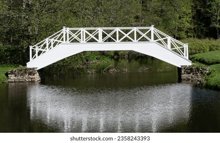 Vihula, Estonia - 20.05.2023: Awesome white wooden bridge crossing a small bond  river. Nice reflection on the water. Warm summer day in Vihula mansion park