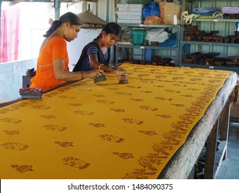 Vijayawada, Andhra Pradesh, India, March 23, 2019: Women workers stamping Kalamkari designs on a yellow sari stretched out on a long table in their workshop. Women empowerment.                      