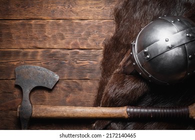 Viking Axe, Helmet And Beast Skin On The Wooden Table Flat Lay Background With Copy Space.