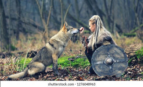 Viking Woman Warrior With Braided Hair Holding Shield Close To Wild Wolf In Forest - Outdoor Warrior Princess Alone In Woods With Wolf – Movie Theme - Cinematic Tone Filter