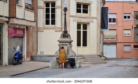 Vilafranca Del Penedès, Spain – September 23, 2021: An Old Lady Collects Water In Vall Del Castell Square In Vilafranca Del Penedès. 