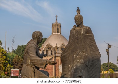 VILLA OF GUADALUPE MEXICO CITY DECEMBER 02 2017. Detail Of A Sculpture Of Juan Diego And Fray Juan De Zumarraga In The Gardens Of The Villa Of Guadalupe. At The Background We Can See The Pocito Church