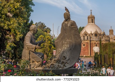 VILLA OF GUADALUPE, MEXICO CITY, DECEMBER 02, 2017. Sculpture Of Juan Diego And Fray Juan De Zumarraga In The Gardens Of The Villa Of Guadalupe. At The Background We Can See The Pocito Church. 