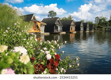 villa on the lakeside with two people rowing a small boat in the water. Clear sky, green trees, and calm water reflection - Powered by Shutterstock