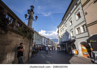 VILLACH, AUSTRIA - SEPTEMBER 13, 2021: Man making phone call with a smartphone on pedestrian street of hauptplatz in Villach, surrounded with shops, stores, in summer. Villach is a city of Carinthia. 