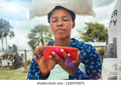 Village African woman carry a bag of rice on her head and is using the cellphone
