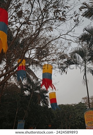 At a village fair, colorful clothes dangle from the branches of a tree, adding vibrancy to the festive atmosphere. The garments sway gently in the breeze, creating a lively and picturesque scene.