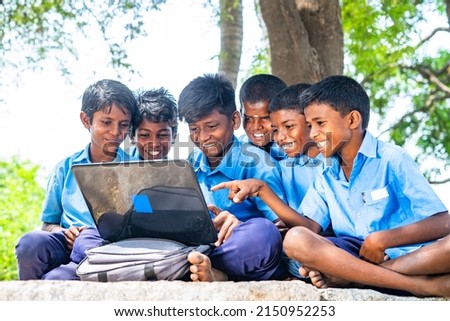 Village group of kids in uniform with using laptop while sitting on near paddy field - concept of education, development and technology.