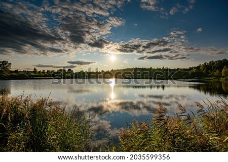 Village pond on the background of a cloudy evening sky with the setting sun