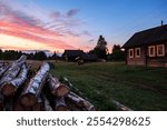 Village at sunset, wooden houses, pink clouds, summer. Sawed birch trees near the house. Scenery.