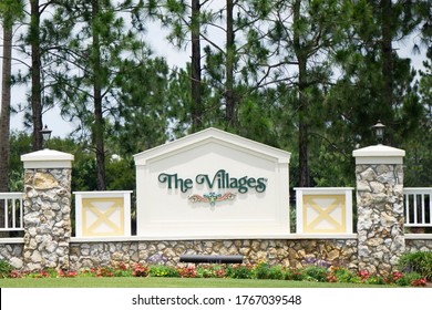 The Villages, Florida/USA - June 2, 2020 -  The Villages Entrance Sign, A Retirement Community, Surrounded By Colorful Flowers, Brick Pillars And Pine Trees On A Sunny Summer Day.