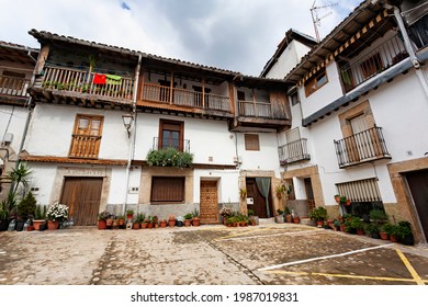 Villanueva De La Vera, Spain - March 08, 2021: Several Old Houses Built In A Traditional Way With Stone Archway At The Front Door And Wooden Beams And Balconies And Lots Of Potted Plants Outside