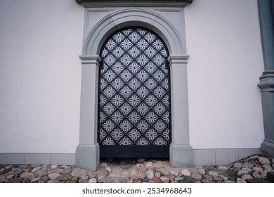 Vilnius, Lithaunia - October 22, 2024 - An ornate, black and white patterned door framed by an arched, gray stone entrance on a building with cobblestone pavement below. - Powered by Shutterstock