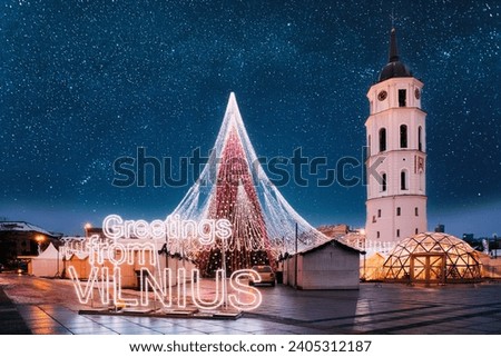 Vilnius, Lithuania. Bell Tower Belfry Of Vilnius Cathedral At Square In Evening New Year Christmas Xmas Illuminations. Amazing Bold Bright Blue Starry Sky Above Christmas Tree On Background.