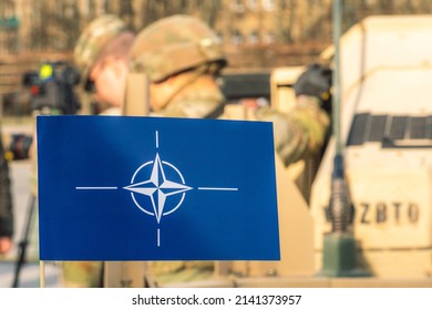 Vilnius, Lithuania - March 29 2022: Flag and symbol of NATO alliance, force integration unit with out of focus group of soldiers and military vehicles on background