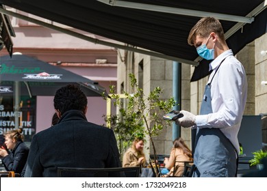 Vilnius, Lithuania - May 15 2020: Waiter With A Mask And Gloves And Client At The Table Of An Outdoor Bar, Cafe Or Restaurant, Reopening After Quarantine, Masks Mandatory