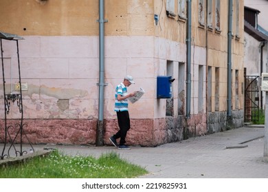 Vilnius, Lithuania - October 12, 2022: Full Body Mature Male In Casual Clothes And Cap Walking Near Shabby Old House And Reading Newspaper On Town Street