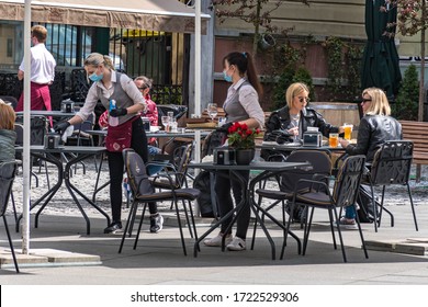 Vilnius, Lithuania - September 15 2021: Beautiful waitresses wearing masks, preparing and disinfecting tables and chairs, outdoor bar, café or restaurant with girls drinking and eating at the table
