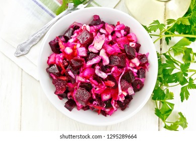 Vinaigrette salad with pickled or sauerkraut, potatoes, beetroot and onions, seasoned with vegetable oil in a bowl, napkin, parsley on a wooden board background from above