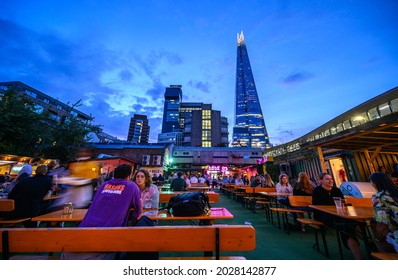 Vinegar Yard, London, UK - Aug 11 2021: Vinegar Yard Is An Open Air Bar Near London Bridge. Customers Enjoy A Drink At The Outdoor Seating Just After Sunset. The Shard And Guy's Hospital Are Behind.