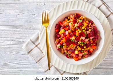 Vinegret, russian vinaigrette, salad of diced cooked red beets, potatoes, carrots, chopped onions, brined pickles, green peas in a white bowl on a white wooden table, flat lay, free space