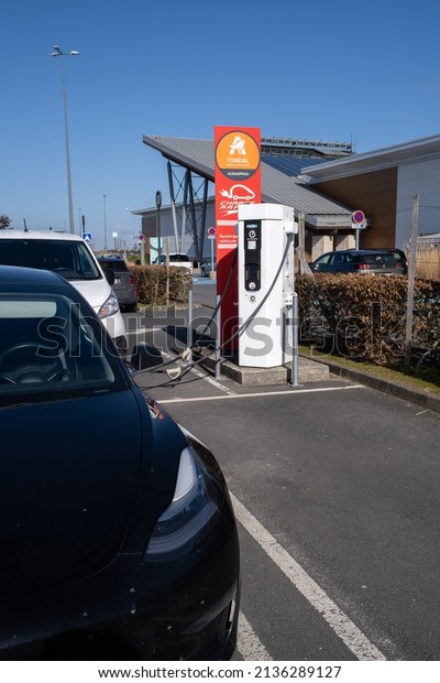 Vineuil, France - February 25, 2022: A static shot\
of a solid black Tesla Model 3 dual motor long range awd charging\
at the AC Auchan charging station in a sunny winter day. Selective\
focus.