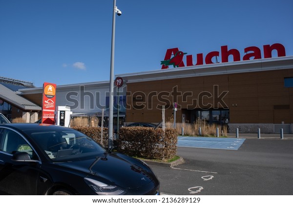 Vineuil, France - February 25, 2022: A static shot\
of a solid black Tesla Model 3 dual motor long range awd charging\
at the AC Auchan charging station in a sunny winter day. Selective\
focus.