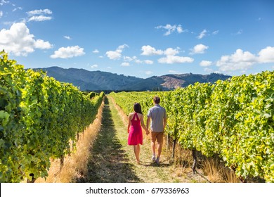 Vineyard couple tourists New Zealand travel visiting winery walking amongst grapevines. People on holiday wine tasting experience in summer valley landscape.