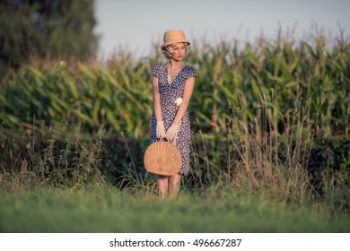 Vintage 1920s Summer Fashion Woman With Blue Dress And Straw Hat Standing With Handbag In Rural Landscape.